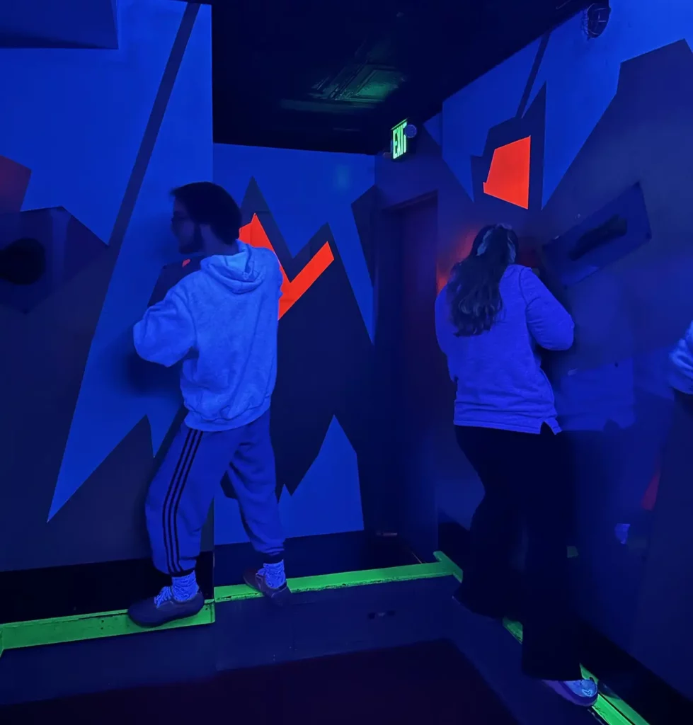 Two people walk against a blue wall